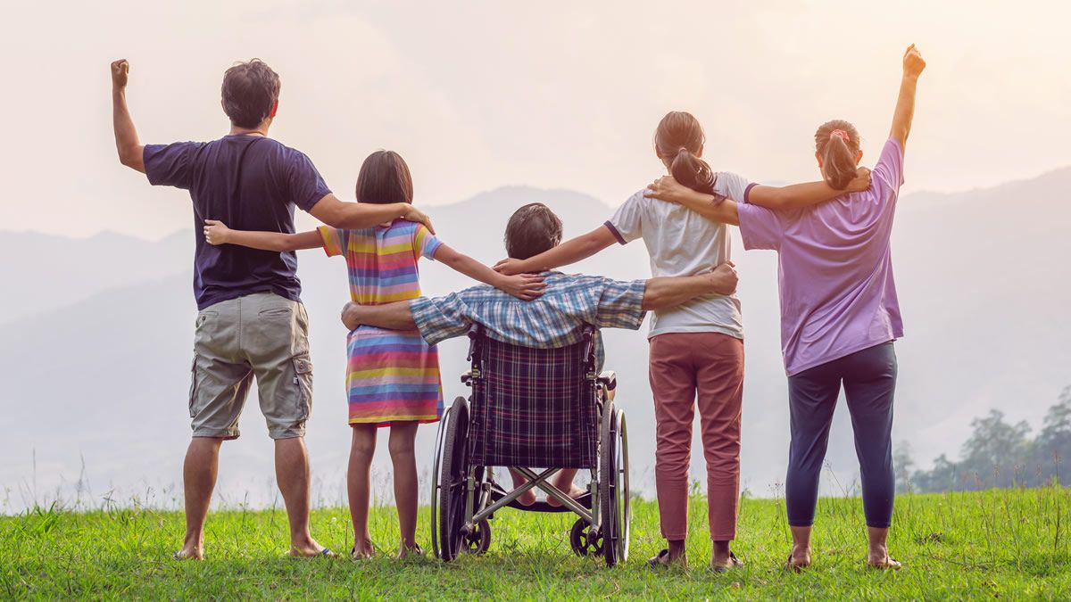 View of family from behind, arms around each other outside, child in wheelchair